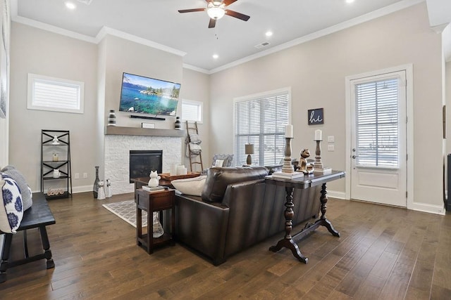 living room featuring dark hardwood / wood-style flooring, crown molding, ceiling fan, and a fireplace