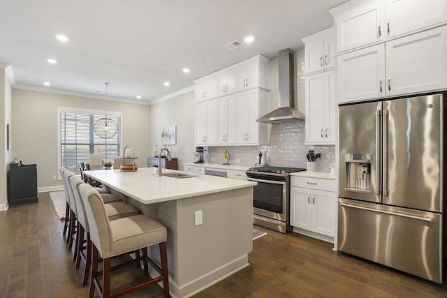 kitchen with sink, appliances with stainless steel finishes, wall chimney range hood, a kitchen island with sink, and white cabinets