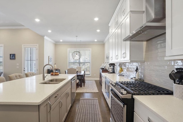 kitchen with sink, wall chimney range hood, an island with sink, stainless steel appliances, and white cabinets