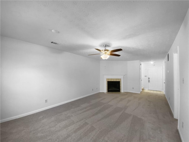 unfurnished living room featuring carpet floors, visible vents, a tiled fireplace, a ceiling fan, and a textured ceiling