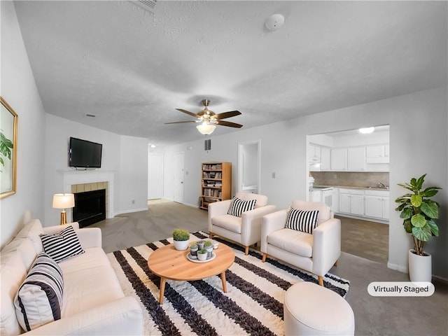 carpeted living room featuring a textured ceiling, a tile fireplace, and a ceiling fan