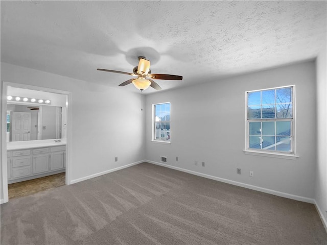 unfurnished bedroom featuring a textured ceiling, carpet flooring, connected bathroom, and baseboards