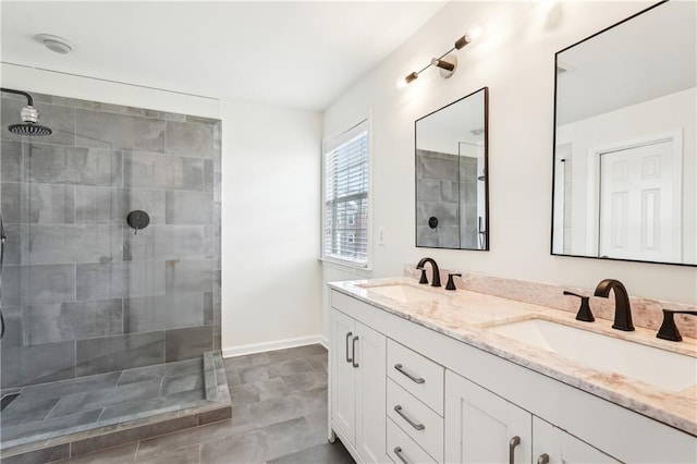 bathroom featuring a sink, baseboards, double vanity, and tiled shower
