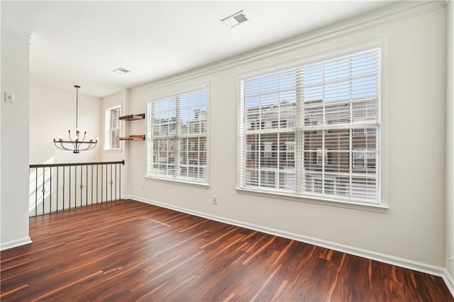 empty room featuring baseboards, an inviting chandelier, wood finished floors, and visible vents