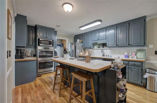 kitchen featuring light hardwood / wood-style flooring, a textured ceiling, tile counters, a kitchen bar, and stainless steel appliances