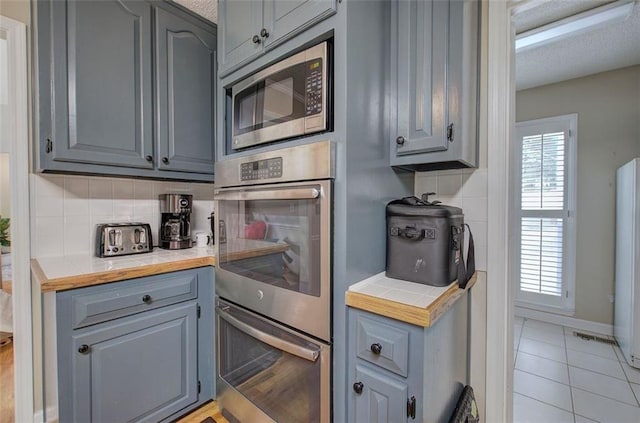 kitchen featuring backsplash, gray cabinets, light tile patterned floors, and appliances with stainless steel finishes