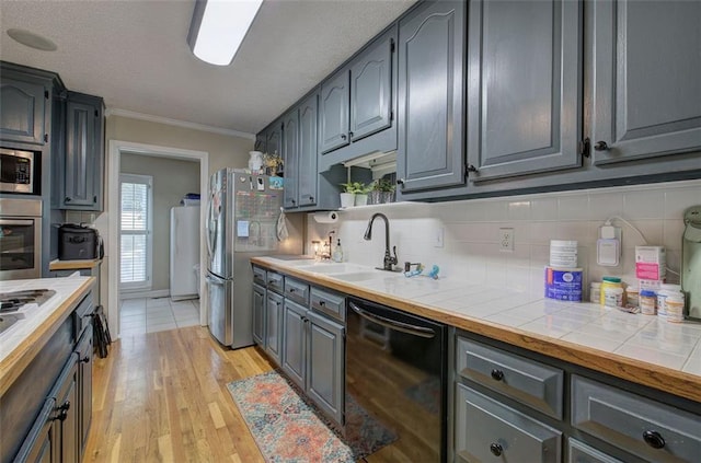 kitchen with crown molding, sink, tile counters, and appliances with stainless steel finishes