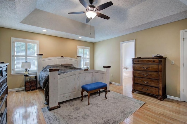 bedroom featuring multiple windows, light wood-type flooring, a raised ceiling, and ceiling fan