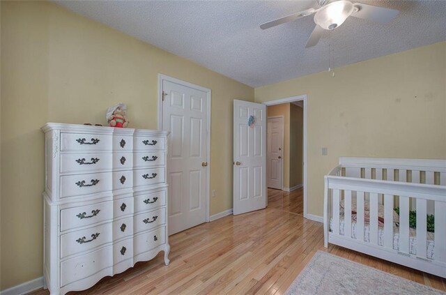 bedroom featuring ceiling fan, light wood-type flooring, a crib, and a textured ceiling