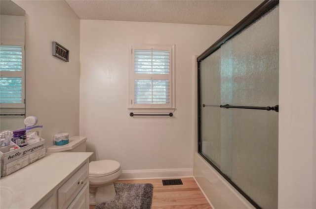 full bathroom featuring bath / shower combo with glass door, vanity, a textured ceiling, wood-type flooring, and toilet