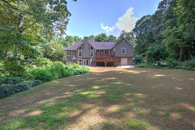 rear view of property featuring a yard, a garage, and a deck