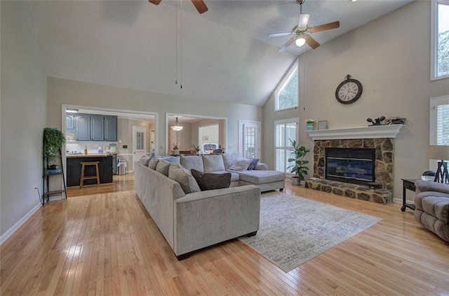 living room with a stone fireplace, ceiling fan, high vaulted ceiling, and light hardwood / wood-style floors