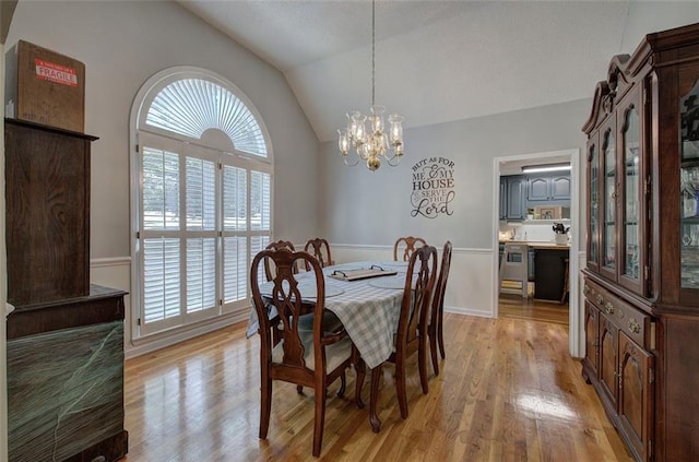 dining space with a chandelier, vaulted ceiling, and light hardwood / wood-style flooring