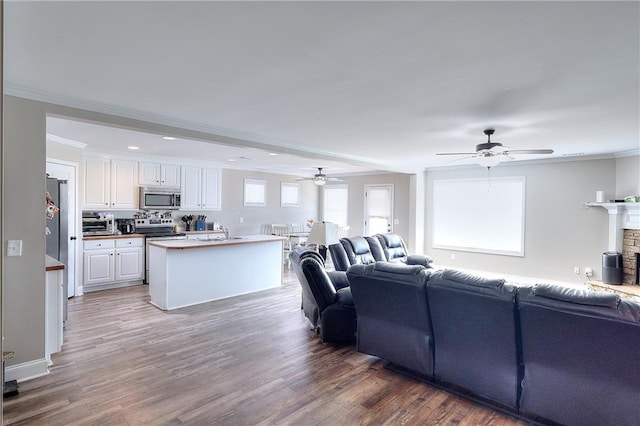 living room featuring crown molding, a stone fireplace, wood-type flooring, and ceiling fan