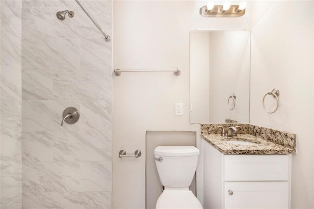 bathroom with toilet, a tile shower, and vanity