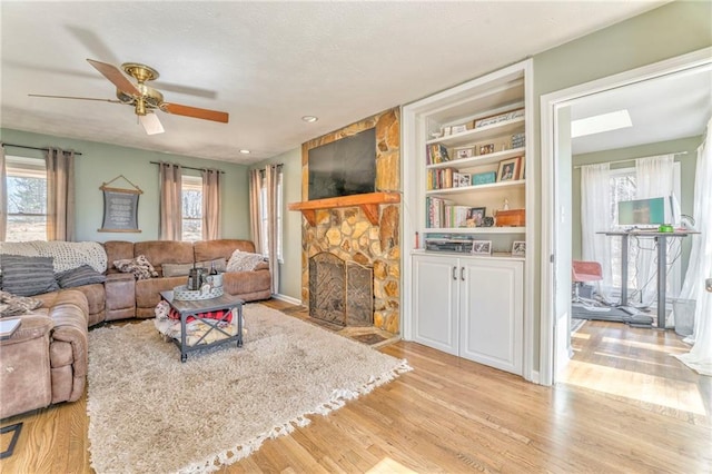 living area with a stone fireplace, ceiling fan, a textured ceiling, and light wood-style floors