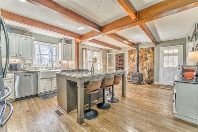 kitchen with visible vents, light wood-style flooring, appliances with stainless steel finishes, a wood stove, and a sink