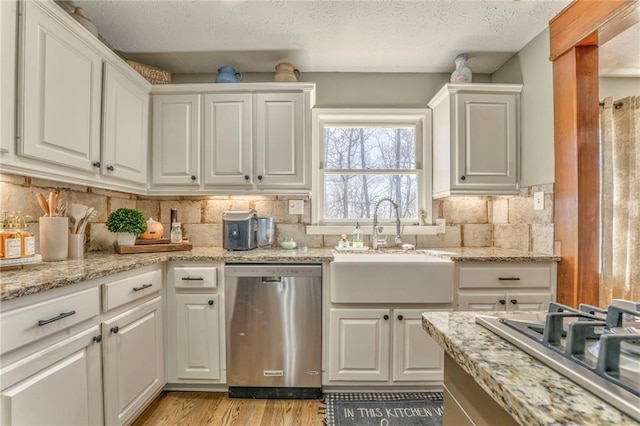 kitchen featuring backsplash, appliances with stainless steel finishes, light wood-style floors, white cabinets, and a sink