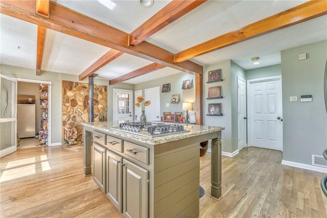 kitchen with a kitchen island, stainless steel gas cooktop, beam ceiling, light wood-style flooring, and a textured ceiling