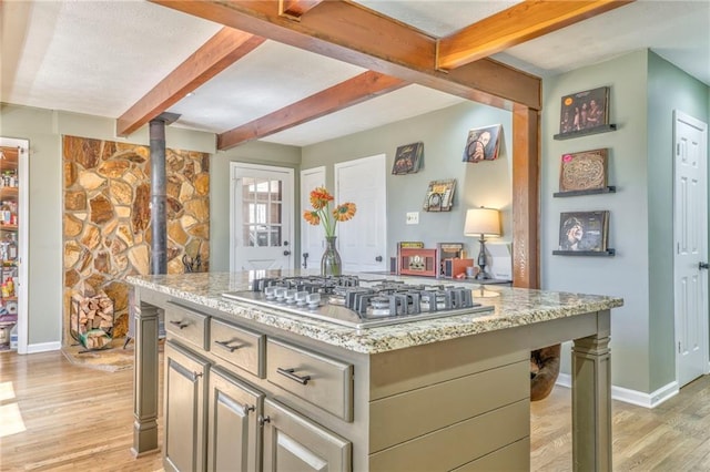 kitchen with a center island, light stone countertops, beamed ceiling, light wood-style floors, and stainless steel gas stovetop