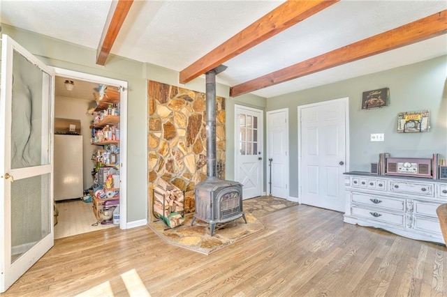 living area with beam ceiling, a textured ceiling, wood finished floors, and a wood stove