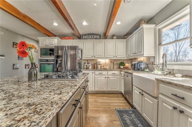 kitchen with light wood finished floors, beam ceiling, decorative backsplash, stainless steel appliances, and white cabinetry