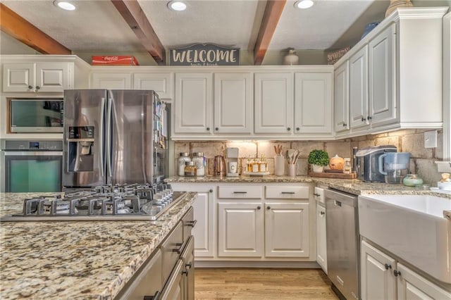 kitchen featuring beamed ceiling, tasteful backsplash, white cabinetry, appliances with stainless steel finishes, and light wood finished floors