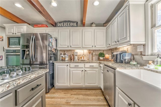 kitchen featuring light wood-type flooring, white cabinets, appliances with stainless steel finishes, beamed ceiling, and tasteful backsplash