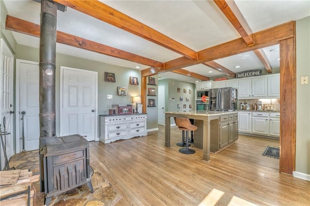 kitchen featuring light wood finished floors, a wood stove, appliances with stainless steel finishes, white cabinetry, and a kitchen bar