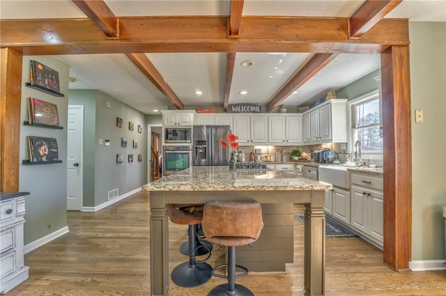 kitchen with a sink, beamed ceiling, light wood finished floors, and stainless steel appliances