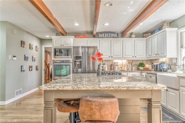 kitchen featuring tasteful backsplash, visible vents, beamed ceiling, appliances with stainless steel finishes, and white cabinetry