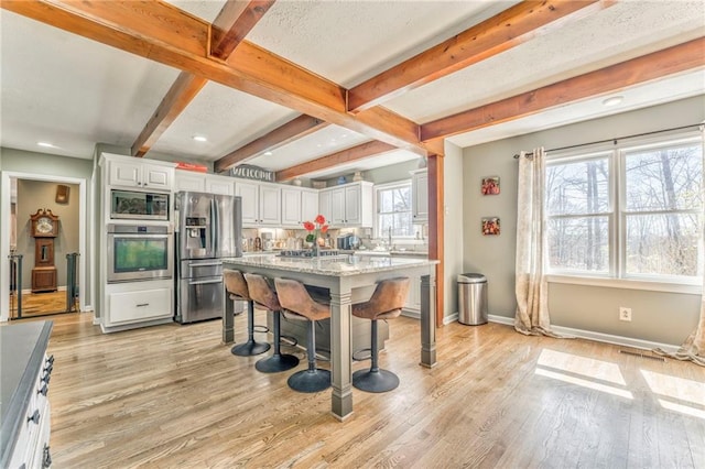 kitchen with light wood-type flooring, a kitchen bar, appliances with stainless steel finishes, and white cabinets