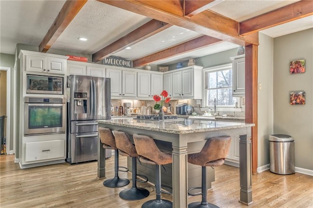 kitchen featuring light wood-type flooring, a kitchen breakfast bar, backsplash, and appliances with stainless steel finishes