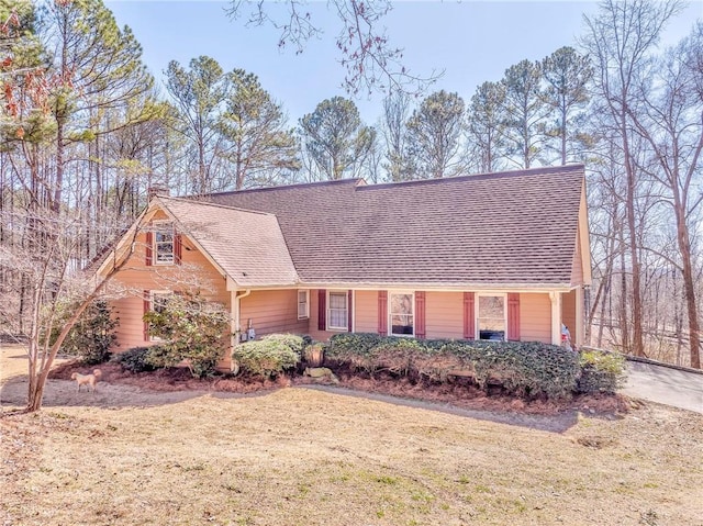 view of front facade featuring a shingled roof and a front yard