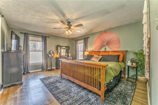 bedroom featuring a ceiling fan, wood finished floors, baseboards, and a textured ceiling