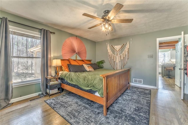 bedroom featuring visible vents, a textured ceiling, baseboards, and wood finished floors