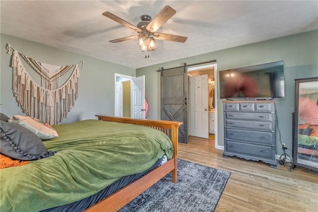 bedroom with a ceiling fan, wood finished floors, baseboards, a textured ceiling, and a barn door