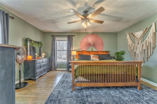 bedroom with baseboards, a textured ceiling, wood finished floors, and a ceiling fan