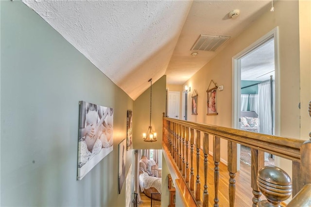 hallway featuring visible vents, lofted ceiling, a textured ceiling, and a notable chandelier