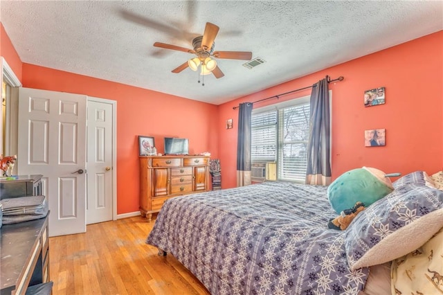 bedroom featuring visible vents, a textured ceiling, light wood-type flooring, and a ceiling fan