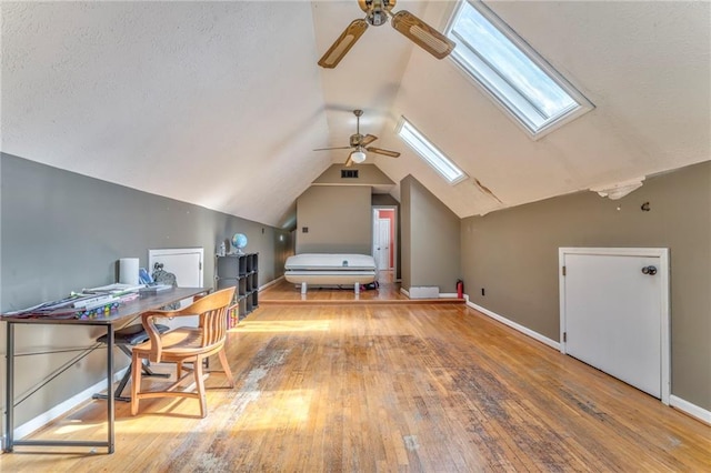 office featuring a textured ceiling, hardwood / wood-style floors, vaulted ceiling with skylight, baseboards, and ceiling fan