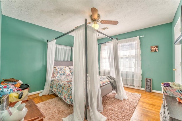 bedroom featuring a textured ceiling, baseboards, light wood finished floors, and ceiling fan