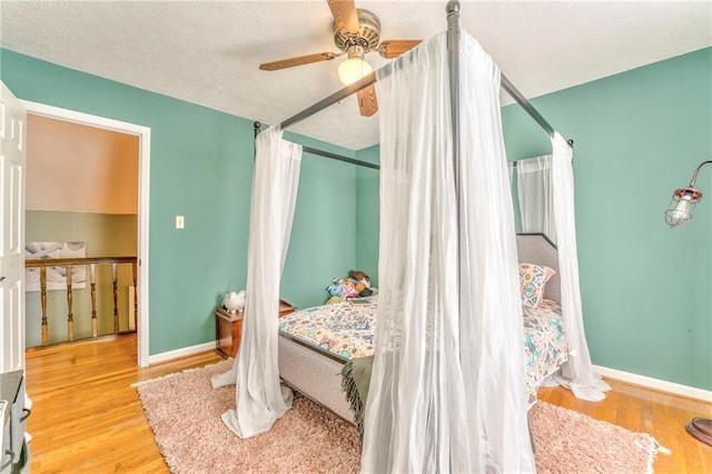 bedroom with a ceiling fan, wood finished floors, baseboards, and a textured ceiling