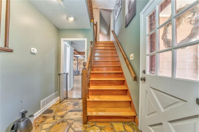 stairway featuring visible vents, a textured ceiling, stone finish flooring, and baseboards