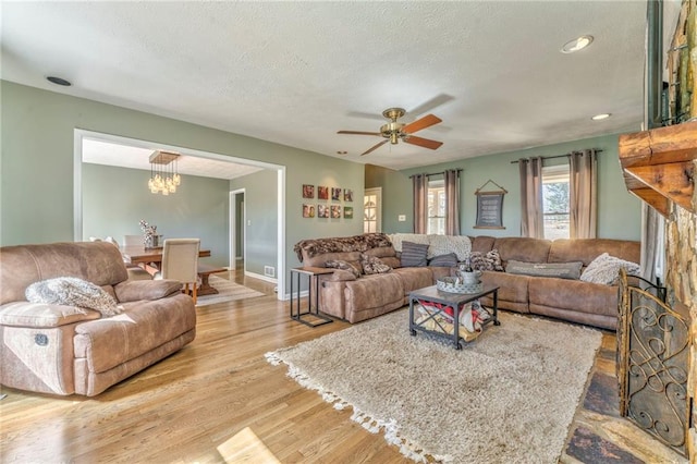 living area with baseboards, a textured ceiling, wood finished floors, and ceiling fan with notable chandelier