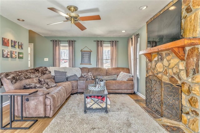 living room with wood finished floors, recessed lighting, a stone fireplace, baseboards, and ceiling fan