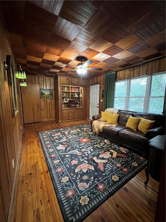 living area with built in features, light wood finished floors, ceiling fan, wood ceiling, and wood walls