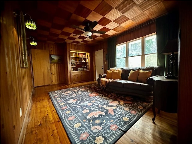 sitting room featuring hardwood / wood-style flooring, wooden walls, built in shelves, and a ceiling fan