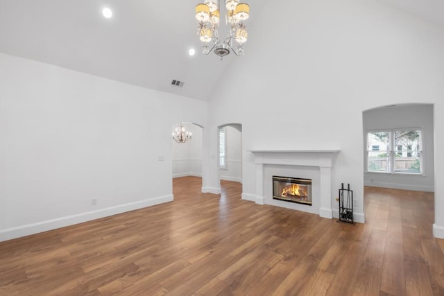 unfurnished living room featuring an inviting chandelier, wood-type flooring, and high vaulted ceiling