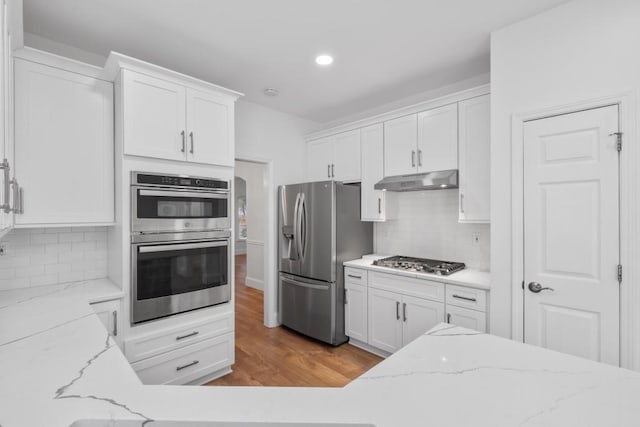 kitchen with white cabinetry, light wood-type flooring, stainless steel appliances, light stone countertops, and decorative backsplash